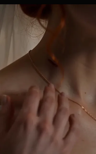 The necklace touch — fingers at her collarbone on a fine chain, the intimacy of the gesture doing all the talking (ep1; romantic-tension frame as aired, not amplified)