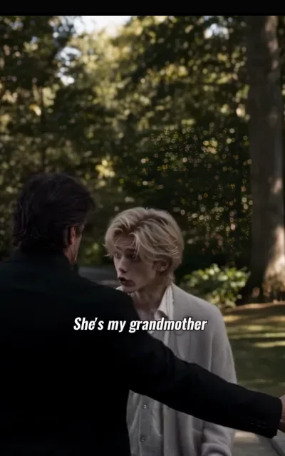 The grounds argument — a dark-haired man in a black coat with an arm out to hold the other back, a light-blond young man in a pale knit cardigan worked up, a faint red mark at his lip, the caption She's my grandmother beneath (ep5; subtitles as aired)