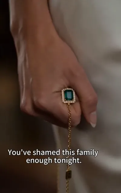 The rebuke - a manicured hand with an emerald-cut ring and a fine gold chain resting against soft fabric in a warm blur (ep2; family-pressure beat - the elder's rebuke scene, marketing not amplified)