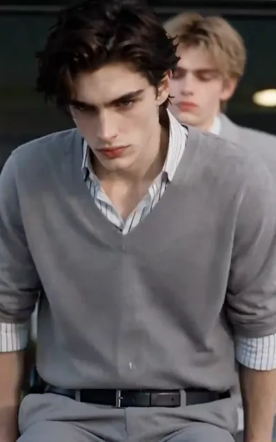 Adrian stares down coldly in his grey knit vest while Noah stands tense behind him