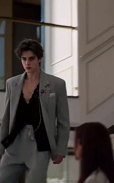 Frame ep02-f01 from episode 2 — Noel walks through the party in his gray suit (ep2; subtitles as aired — Do you see it clearly? Now, she's the one suited to stand beside Adrian.)