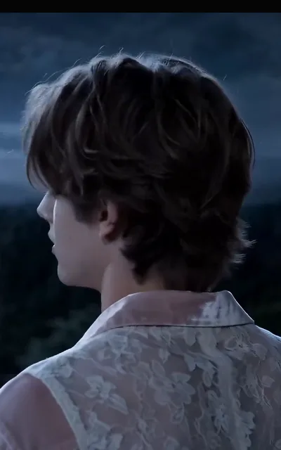 A deep-brown-curled guest in an ornate sleeveless top with delicate open-work detailing, identity unrevealed by the frame — a household presence with no name attached; he stays unnamed (ep1; platform design choice, recorded as aired)