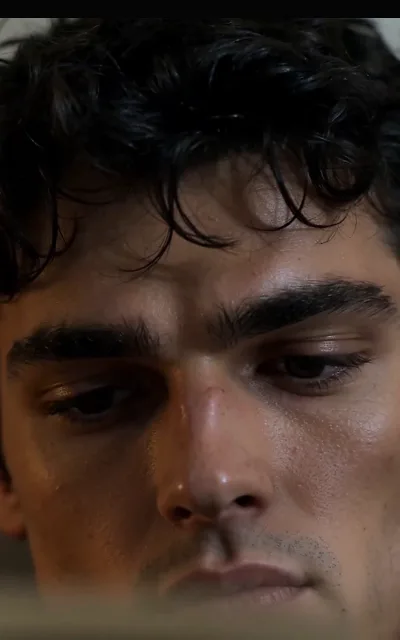 Kael in a sweat-beaded close-up, dark curls damp at the brow and eyes down — the weight of the arc settling on the roommate who carries the secret (ep4)