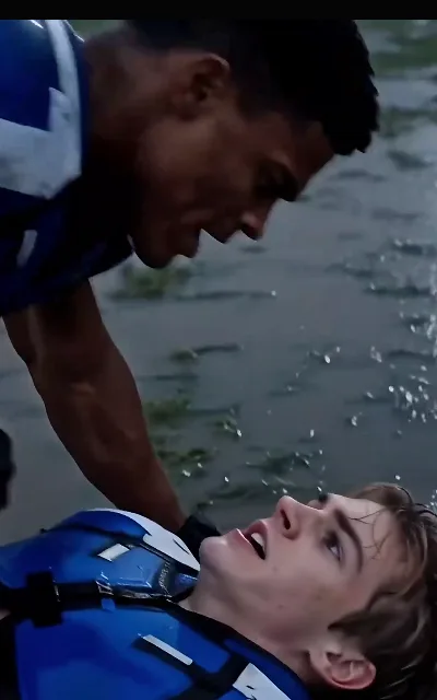 The rainy scrap — the receiver flat on the rain-soaked ground looking up mid-breath, the quarterback bent over him in matching kit, mud and flying water between them (ep5)
