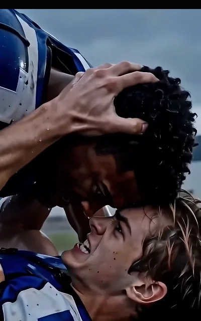 The celebration frame — a hand on the helmet, forehead to forehead, the receiver’s mud-flecked grin open wide under the rain-gray sky; the source of this page’s key art (ep5)