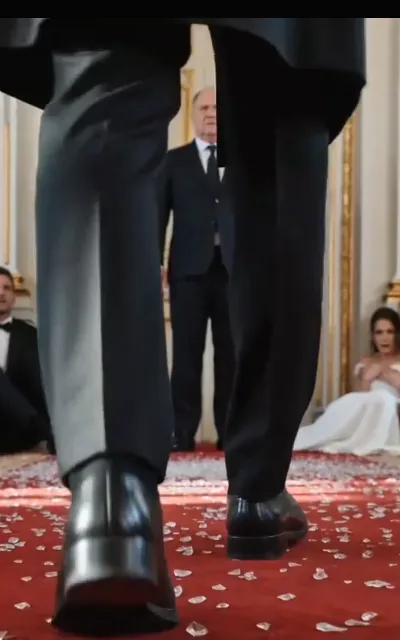 The wedding, low angle — two figures in black above a bride in white collapsed onto the aisle, the veil pooled around her, guests a blur behind (ep2; atmosphere beat)