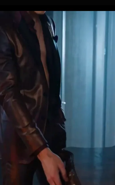 The leather portrait — a glossy chestnut leather jacket worn open, warm light tracing the grain, one hand hanging easy with a little motion blur, cold blue verticals behind (ep8; intimacy-adjacent frame as aired, not amplified — torso study, no second person)