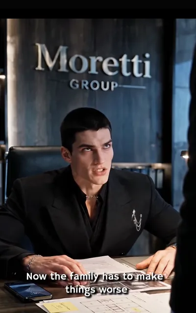 Dante at the office — all black, chain bracelet, drawings and papers spread on the desk, the Moretti GROUP lettering on the wall behind — "Now the family has to make things worse" (ep4; station caption as aired in frame, NOT a quote card; in-story family-group signage kept as aired, no character surnames assigned)