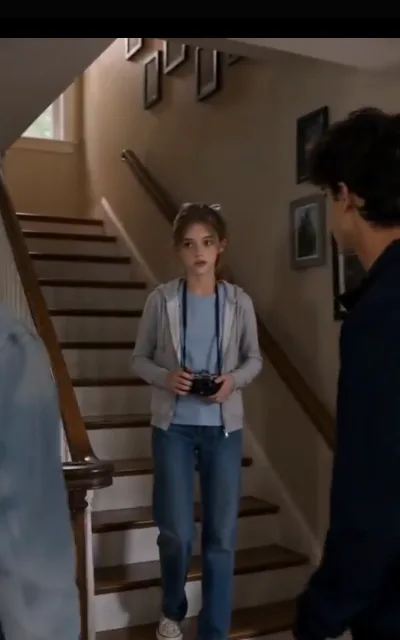 The series’ opening family memory — an earlier household, the home stairway, a first camera held in both hands, a brother-shaped figure passing in the foreground; a background frame kept for the family narrative, not used as key art or avatar (ep1)