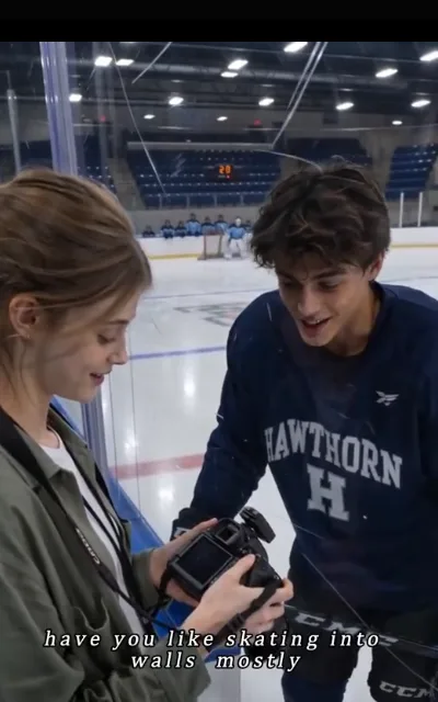Piper holding her camera screen up across the boards for Grant in training kit to see — "have you like skating into walls mostly" (ep3, subtitles as aired)