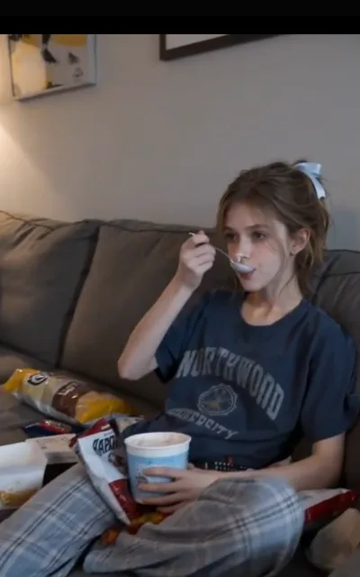 A night in with ice cream — Piper on the couch in a college tee, spoon mid-air, snacks and a family-size tub around her (ep5)