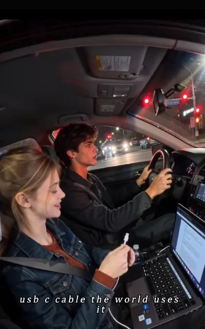 A red light and a charge cable — Piper holding up the cable for the dying laptop, grinning mid-explanation (ep8)