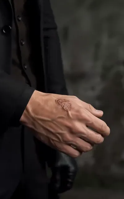 A black-suited hand close up, a rose tattoo in relief across its back — the mark of the Iron Wolf Gang's second-in-command, and this page's anchor for Dante's look (ep1)