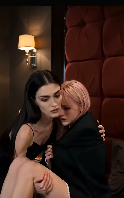 Blair wrapped around Beatrice under the wall-lamp light, the fear-of-dark night watch turned tender — the GL register the whole free run has been pulling toward (ep5; intimate frame as aired, no explicit content)