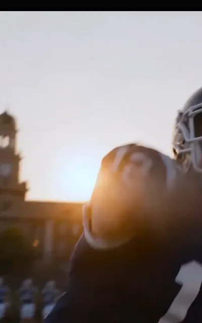 The ball against the sunset — a helmet at the frame edge, a football lifted into golden backlight, the campus clock tower out of focus behind (ep5; atmosphere beat)