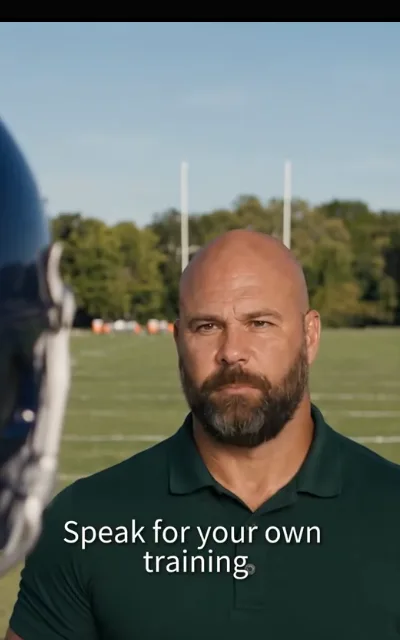 The coach on the grass — forest-green polo, beard, goalposts behind — “Speak for your own training” (ep9; subtitles as aired)