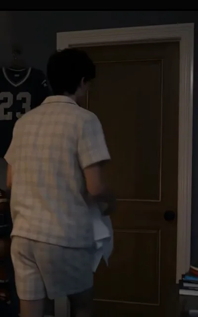 Pajamas at the door — plaid sleep set, a pale shirt clutched in one fist, a number-23 jersey hanging on the wall (ep10; atmosphere beat; the wall jersey 23 is a different one from the number-12 proof jersey)