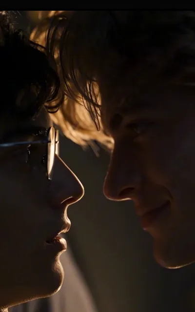 Nose to nose in the warm dark — one in glasses, one lit gold at the edges, neither backing away (ep10; HERO SOURCE)