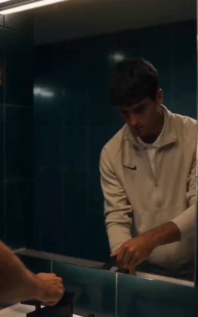 The mirror — a player alone in a low-lit washroom, collar up, weighing everything the press conference just dragged back up (ep2)